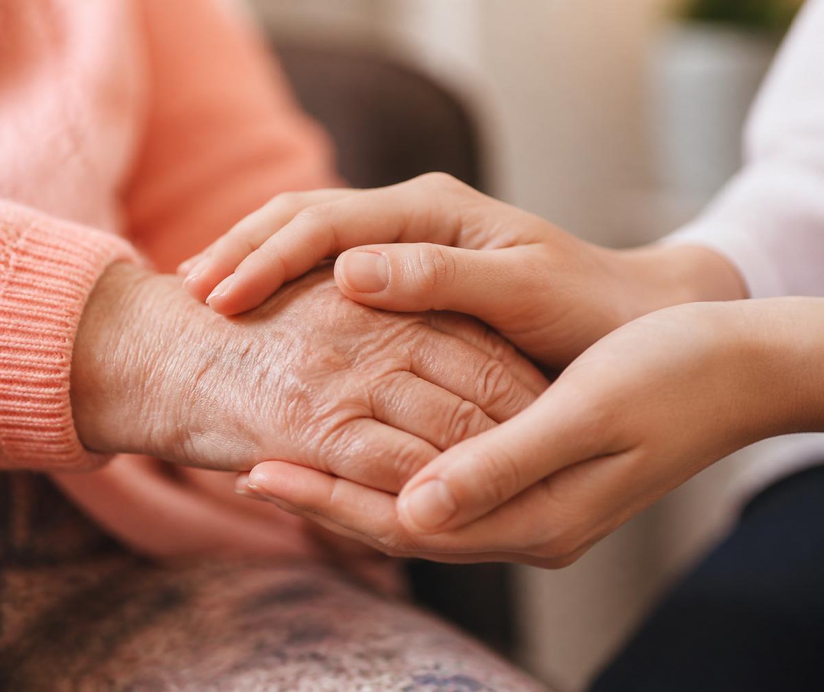 Two hands gently helping an elderly person step out of a vehicle